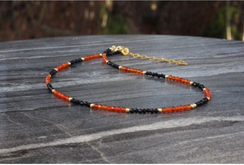 Puede incluir: Un collar delicado con cuentas negras y naranjas alternas. El collar est&aacute; hecho con cuentas peque&ntilde;as y redondas y tiene un cierre de cadena dorada.