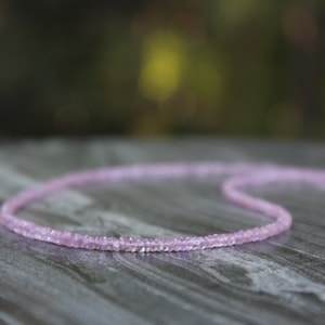 May include: A delicate pink gemstone necklace with a gold clasp. The necklace is made of small, faceted gemstones that are strung together on a thin chain.