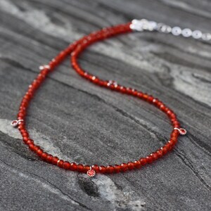 Puede incluir: Un collar de piedras preciosas de cornalina roja con detalles plateados. El collar est&aacute; hecho de peque&ntilde;as cuentas redondas y tiene un aspecto delicado y femenino.