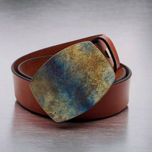 Può includere: Una cintura in pelle marrone con una fibbia in metallo unica e colorata. La fibbia presenta un motivo marmoreo blu, verde e oro.