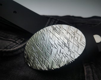 May include: A silver belt buckle with a textured, geometric design. The buckle is oval shaped and has a brushed finish.