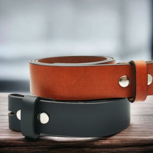 May include: Two leather belts, one brown and one black, with metal buckles. The belts are stacked on top of each other.