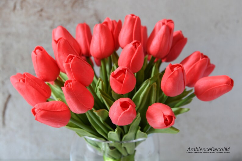 May include: A bouquet of red artificial tulips in a clear glass vase. The tulips are arranged in a cluster, with the stems extending out from the vase. The tulips are a vibrant red color, and the vase is clear glass.