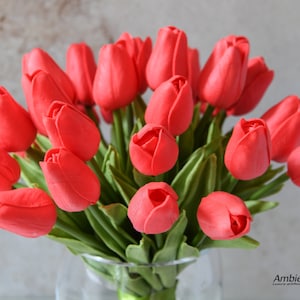 May include: A bouquet of red artificial tulips in a clear glass vase. The tulips are arranged in a cluster, with the stems extending out from the vase. The tulips are made of a soft, realistic material.