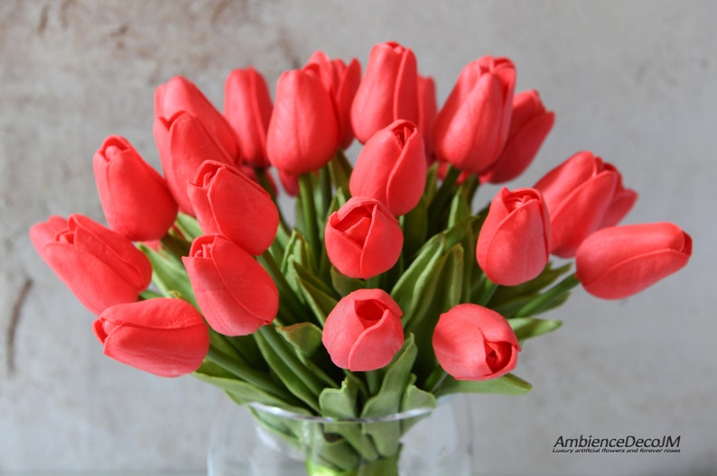 May include: A bouquet of red artificial tulips in a clear glass vase. The tulips are arranged in a cluster, with the stems extending out from the vase. The tulips are made of a soft, realistic material.