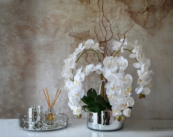 May include: White orchid flower arrangement in a silver mirrored vase with a silver tray and a glass bottle of diffuser sticks.
