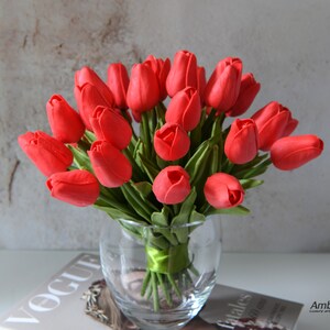 May include: A bouquet of red tulips arranged in a clear glass vase. The vase is sitting on a magazine with the word "Vogue" visible.