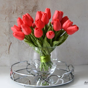 May include: A bouquet of red tulips arranged in a clear glass vase with a green ribbon. The vase is sitting on a silver tray with a mirrored surface.