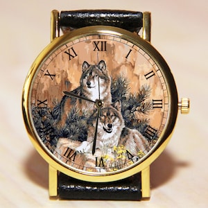 May include: A gold-tone wristwatch with a black leather band. The watch face features a detailed illustration of two wolves in a forest setting with Roman numeral hour markers.