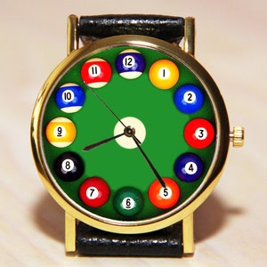 May include: A gold-tone wristwatch with a green face and billiard ball hour markers. The watch has a black leather band.