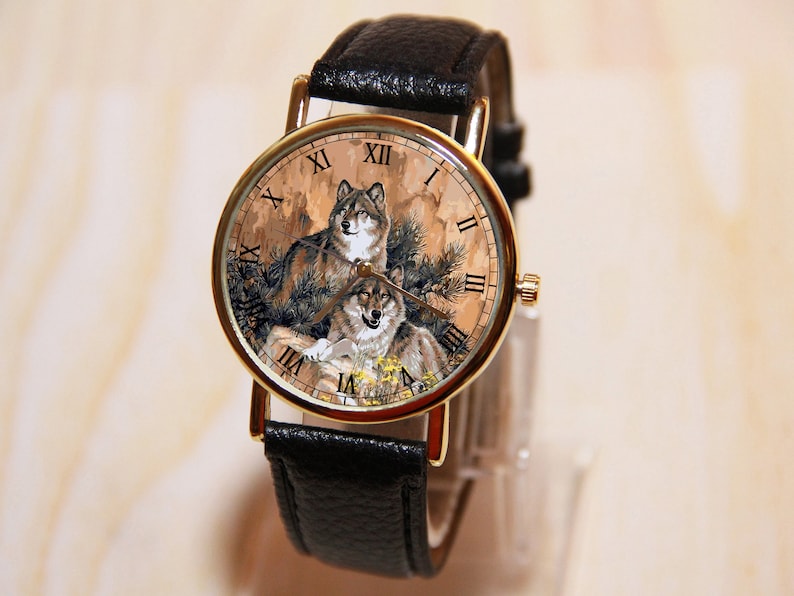 May include: A gold-tone wristwatch with a black leather band. The watch face features a brown and tan background with a painted image of two wolves. The Roman numeral hours are black.