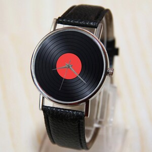 K&ouml;nnte beinhalten: Eine schwarze Lederarmbanduhr mit einem silbernen Geh&auml;use und einem schwarzen und roten Vinyl-Platten-Design auf dem Zifferblatt.