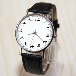 May include: A silver wristwatch with a white face and black leather band. The numbers on the face are in Japanese characters.