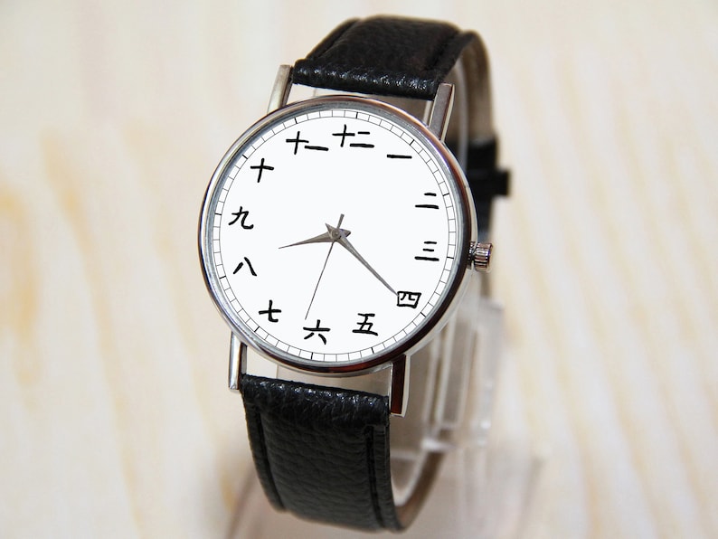 May include: A silver wristwatch with a white face and black leather band. The numbers on the face are in Japanese characters.