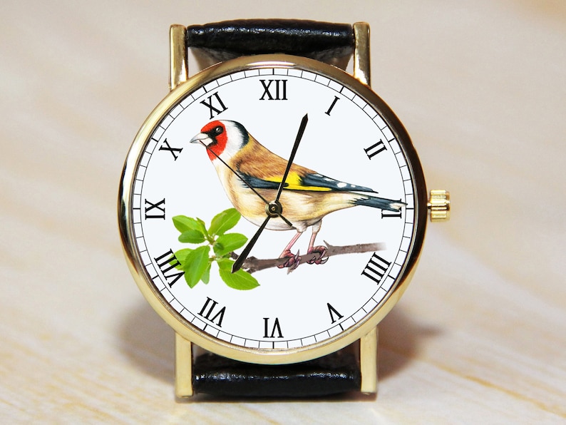Peut inclure: Montre-bracelet dor&eacute;e avec un bracelet en cuir noir. Le cadran pr&eacute;sente une illustration d&eacute;taill&eacute;e d'un chardonneret perch&eacute; sur une branche avec des feuilles vertes. Chiffres romains.