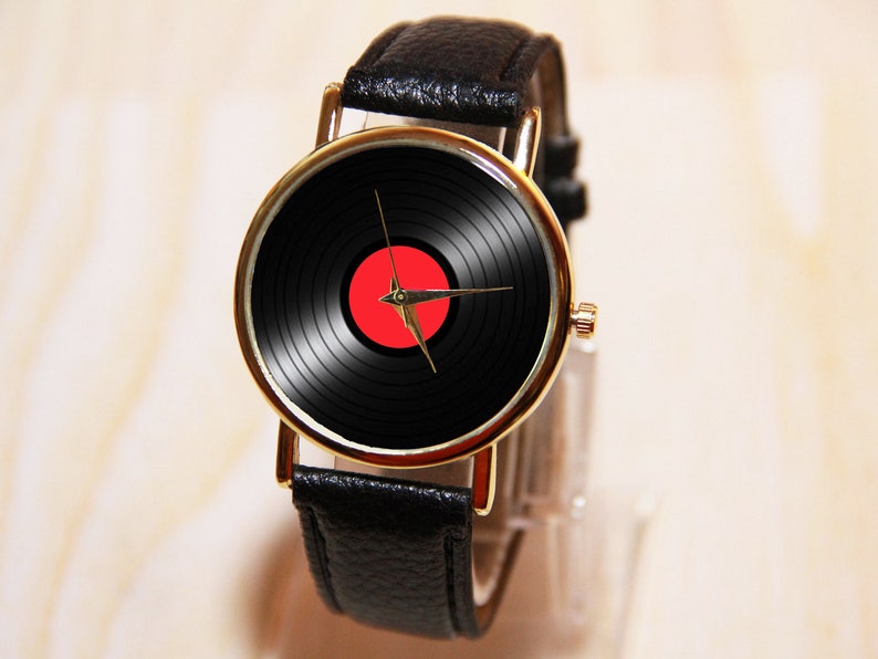 May include: A gold-tone wristwatch with a black leather band. The watch face features a black and red vinyl record design.
