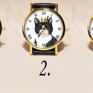 Op de afbeelding: Drie goudkleurige polshorloges met zwarte leren bandjes. Elk horloge heeft een zwart-witte kat met een ander ontwerp: een strikje, een gouden kroon en een bloemenkroon.
