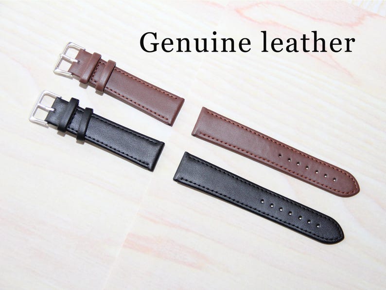 May include: Two leather watch straps, one brown and one black, with silver buckles. The straps are laid out on a white surface. The text "Genuine leather" is visible above the straps.