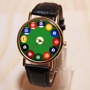 May include: A black leather wristwatch with a gold-tone case and a green face. The face of the watch is decorated with billiard balls numbered 1 through 12.