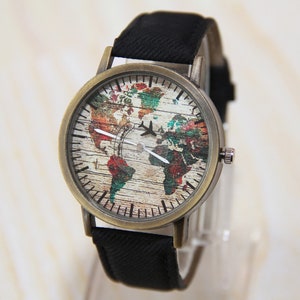 May include: A vintage-style wristwatch with a black canvas band and a round, brass-colored case. The watch face features a colorful world map with a woodgrain texture and a small airplane icon.