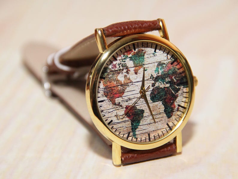 May include: A gold-tone wristwatch with a brown leather band. The watch face features a world map design with a white background and colorful continents.