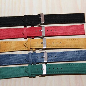 May include: Five watch straps in different colours: black, red, yellow, blue, and green. The straps are made of a textured fabric and have silver buckles.