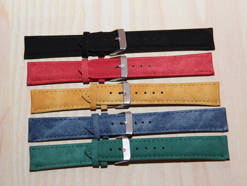 May include: Five watch straps in different colours: black, red, yellow, blue, and green. The straps are made of a textured fabric and have silver buckles.