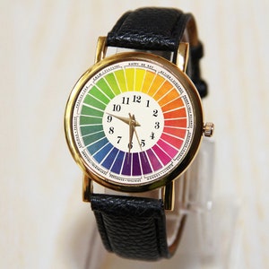 Puede incluir: Un reloj de pulsera dorado con una correa de cuero negro. La esfera del reloj presenta una rueda de colores arco&iacute;ris con los n&uacute;meros del 1 al 12 alrededor del borde.