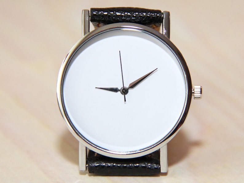 Pu&ograve; includere: Un orologio argentato con quadrante bianco e cinturino in pelle nera.