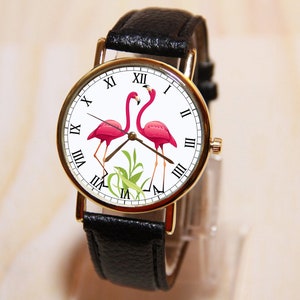 May include: A black leather wristwatch with a white face and gold accents. The face features two pink flamingos and Roman numeral hour markers.