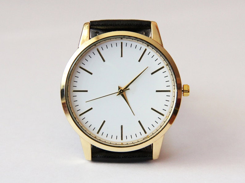Puede incluir: Un reloj de pulsera dorado con una esfera blanca y una correa de cuero negra.