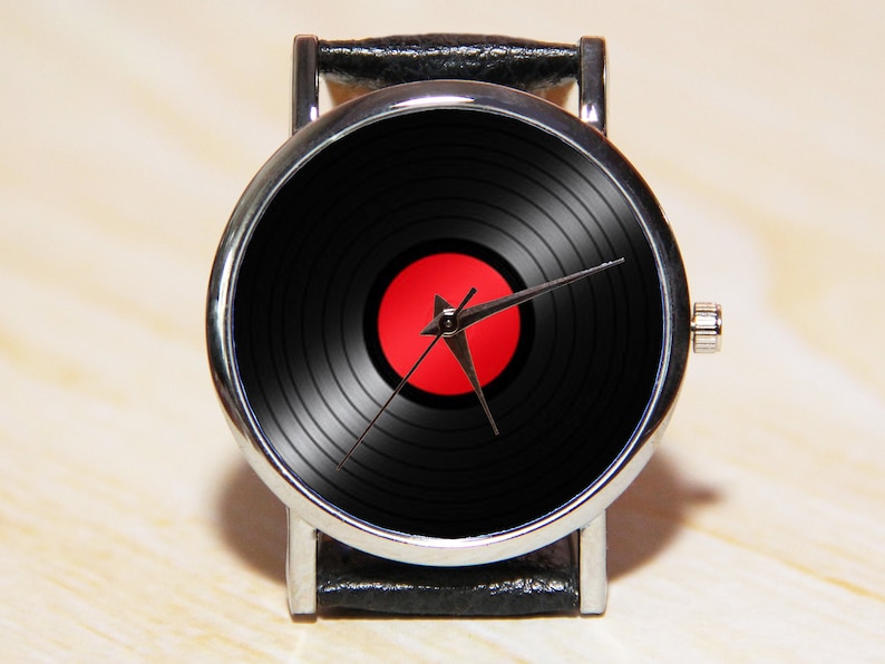May include: A silver wristwatch with a black leather band. The watch face features a black vinyl record design with a red center label.