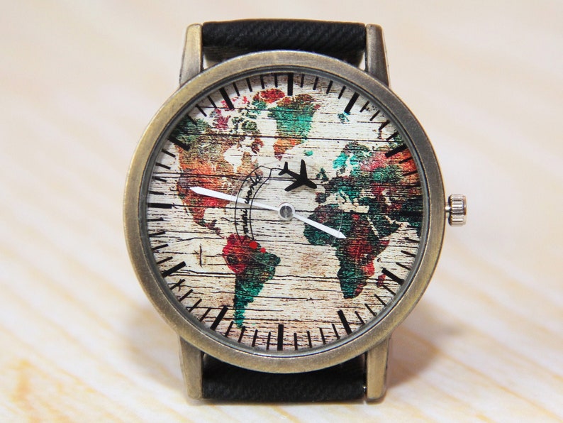 May include: A vintage-style wristwatch with a black leather band and a round, brass-colored case. The watch face features a colorful world map with a small airplane graphic.