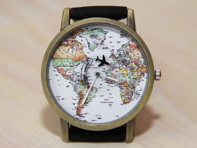 May include: A vintage-style wristwatch with a black leather strap and a round, gold-toned case. The watch face features a detailed world map with a small aeroplane icon and the words "Around the World" printed on the face.