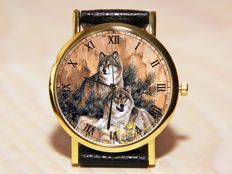 May include: A gold-tone wristwatch with a black leather band. The watch face features a detailed illustration of two wolves in a forest setting with Roman numeral hour markers.