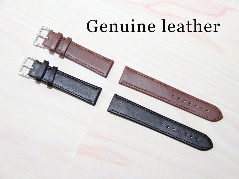 Puede incluir: Dos correas de reloj, una marr&oacute;n y otra negra, hechas de cuero genuino. Ambas correas tienen costuras y se muestran sobre una superficie de madera clara.