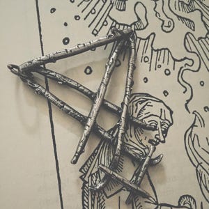 May include: A silver pendant in the shape of a triangle made from intertwined branches. The pendant is on a white background with a black and white illustration.