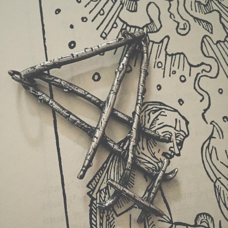 May include: A silver pendant in the shape of a triangle made from intertwined branches. The pendant is on a white background with a black and white illustration.
