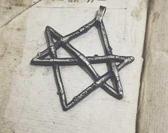 May include: A silver-toned metal pendant in the shape of a five-pointed star. The star is made of interwoven branches, creating a rustic and organic look.