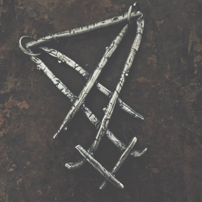 May include: A silver pendant in the shape of a triangle with a textured surface. The pendant is made of multiple interwoven metal strips.