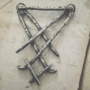 May include: A silver pendant necklace featuring a design of three intertwined branches. The branches are textured to resemble birch bark.