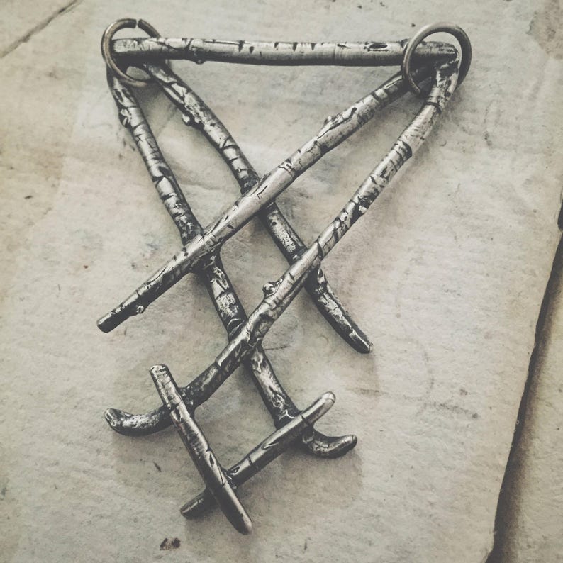 May include: A silver pendant necklace featuring a design of three intertwined branches. The branches are textured to resemble birch bark.