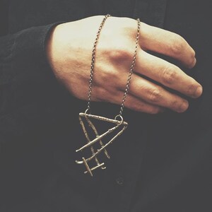 May include: A silver necklace with a geometric pendant made of thin, interwoven metal bars. The pendant is in the shape of a triangle.