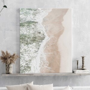 May include: An aerial photograph of a sandy beach with turquoise water crashing on the shore. The image is taken from a high angle, showing the waves breaking and the sand stretching out to the horizon.