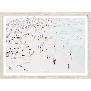 May include: An aerial view of a crowded beach with people swimming, sunbathing, and walking along the shore. The water is a light blue color and the sand is white. The image is taken from a high angle, giving a bird's eye view of the beach.