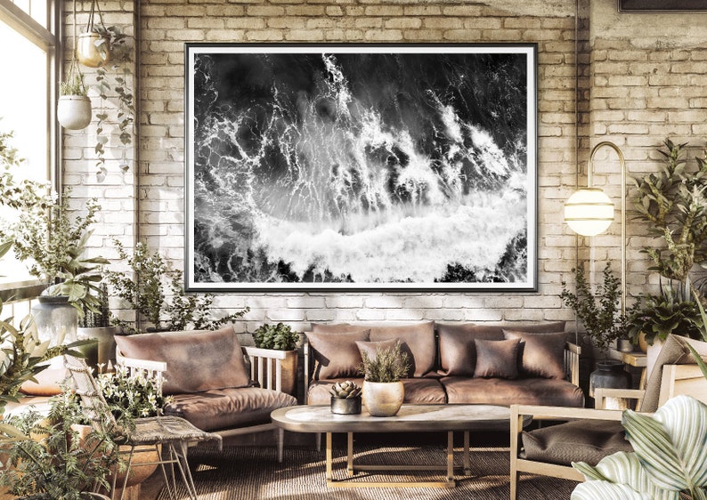 Puede incluir: Una fotograf&iacute;a en blanco y negro de olas rompiendo enmarcada en un marco negro cuelga de una pared de ladrillo en un ambiente de sala de estar. La habitaci&oacute;n cuenta con un sof&aacute; de cuero marr&oacute;n, una mesa de caf&eacute; y plantas.