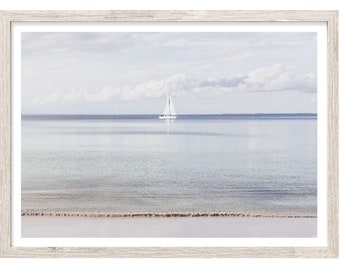 May include: A framed wall art print featuring a single white sailboat on a calm, light blue ocean under a soft, cloudy sky. The scene captures a serene horizon line where the water meets the sky, enclosed in a light-toned, weathered wood frame.