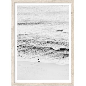 May include: A black and white photograph of a person walking on a sandy beach with waves crashing in the background.