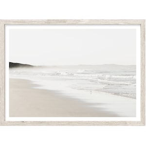 May include: A framed photograph of a beach scene with white sand, foamy waves, and a distant coastline. The image is in muted tones of white, gray, and beige.