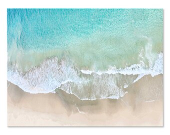May include: An aerial view of a sandy beach with turquoise water and white foamy waves crashing on the shore.